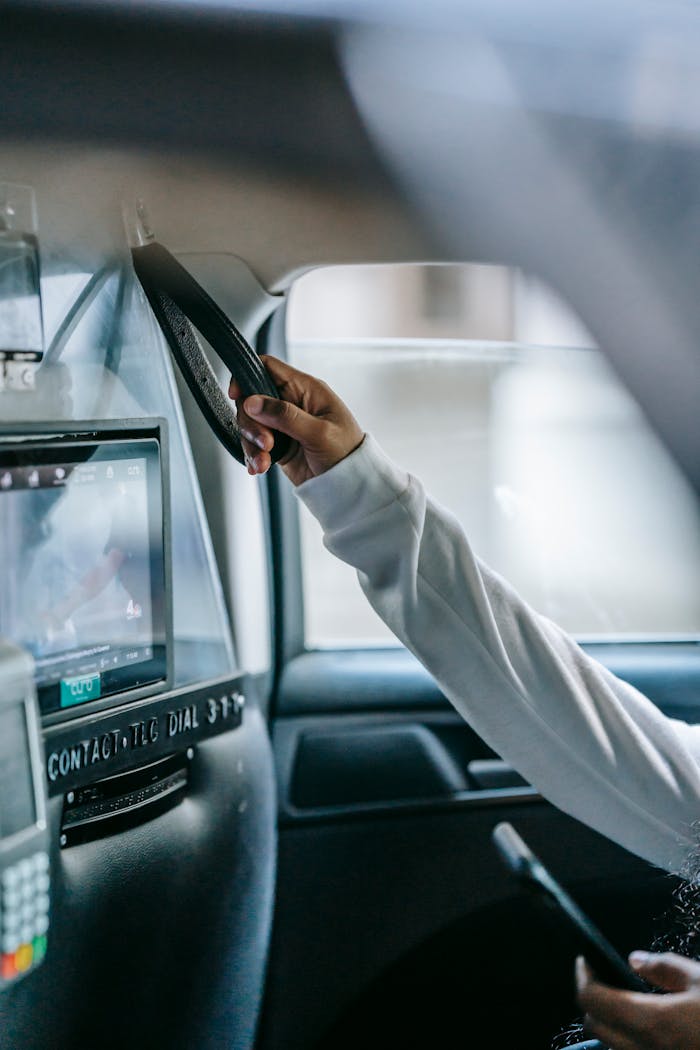 Crop anonymous African American female passenger holding hanging handle and messaging on smartphone while sitting in taxi