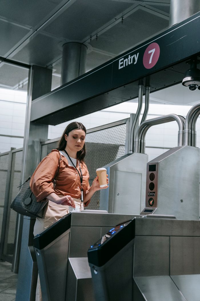 A woman holding a coffee cup passes through a subway station turnstile.